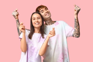 Genç çift pembe arka planda parmakları olan kalpler yapıyor.