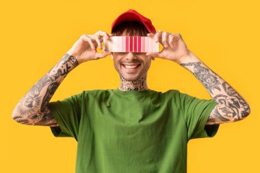 Sarı arka planda palet örnekleriyle yüzünü kapatan genç adam.