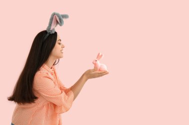 Paskalya tavşanı kulaklı, pembe arka planda oyuncak tavşanı olan güzel, genç bir kadın.