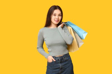 Sarı arka planda alışveriş torbaları olan şık giyimli, şık Asyalı bir kadın.