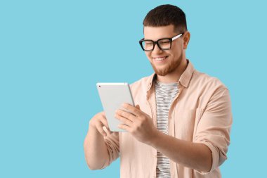 Mavi arka planda tablet bilgisayar kullanan gözlüklü genç adam.