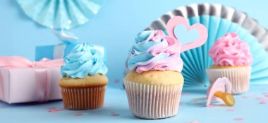 Lezzetli kekler, emzik, hediyeler ve açık mavi arka planda kağıt kalp. Cinsiyet gösterme partisi afişi 