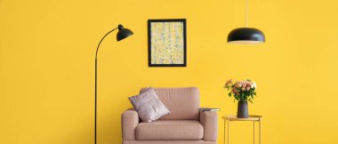 Masanın üzerinde bir buket taze gül ve sarı duvarın yanında lambalar olan rahat bir koltuk.