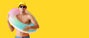 Sarı zemin üzerinde şişirilebilir halkası olan çekici genç bir adam ve metin için yeri var.