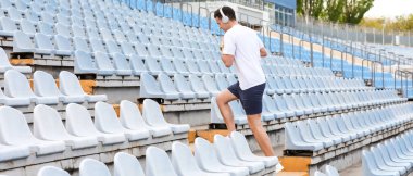 Stadyumun üst katında kulaklıklı genç bir adam koşuyor.