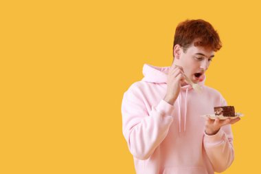 Sarı arka planda doğum günü pastası yiyen genç adam.