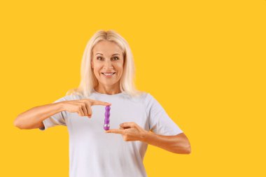 Sarı arka planda vibratörü olan olgun bir kadın.