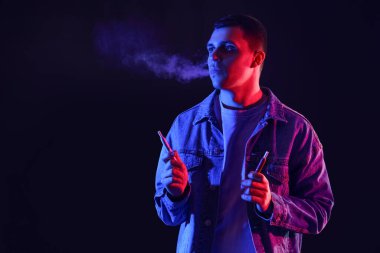 Siyah arka planda elektronik sigara içen genç adam.