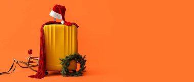 Bavul, Noel Baba şapkası, Noel çelengi ve turuncu arka planda kızak. Mesaj için yer var. Kış yolculuğu konsepti