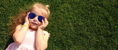 Yeşil çimlerin üzerinde uzanmış güneş gözlüklü şirin bir kız. Tasarım için pankart