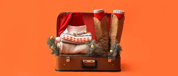 Koffer Mit Nikolausmütze Warmer Kleidung Und Weihnachtsbaumzweigen Auf Orangefarbenem Hintergrund lizenzfreie Stockbilder