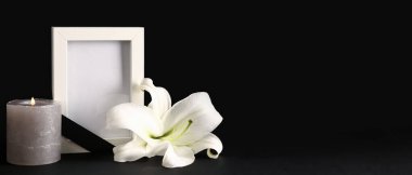 Zambak çiçeği, boş cenaze çerçevesi ve koyu arkaplanda yanan mum.