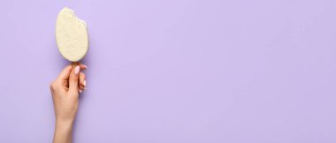 Lezzetli beyaz çikolata kaplı, eflatun arkaplanlı ve metin için yeri olan kadın eli.