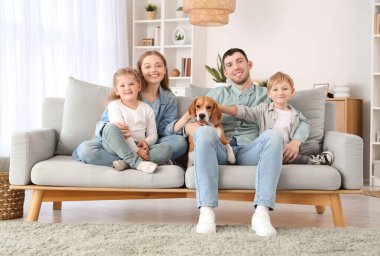 Anne babaları ve Beagle köpeği olan küçük çocuklar evdeki kanepede oturuyorlar.