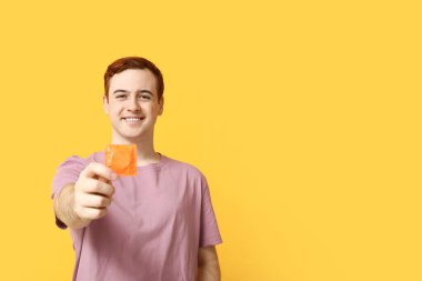 Sarı arka planda prezervatifli genç bir adam. Güvenli seks konsepti