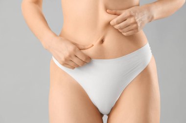 Gri arka planda göbek selülit sorunu olan iç çamaşırlı güzel bir kadın.