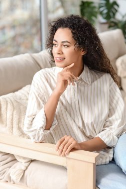 Young African-American woman sitting on sofa at home