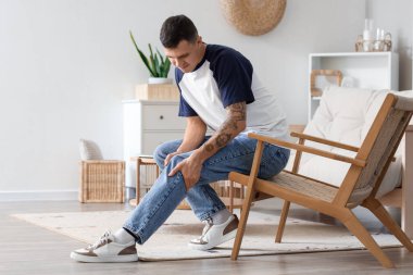 Evdeki sandalyede diz ağrısı çeken genç bir adam.