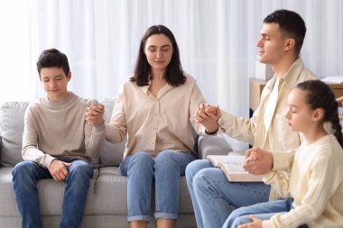 İncil 'i olan bir aile evdeki kanepede dua ediyor.