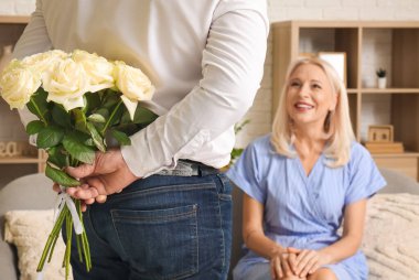 Evdeki sevgili karısı için gül buketi taşıyan olgun bir adam.