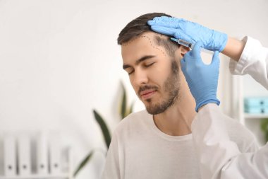 Alnı işaretli genç adam hastanede saç büyümesi için iğne oluyor, yakın plan.