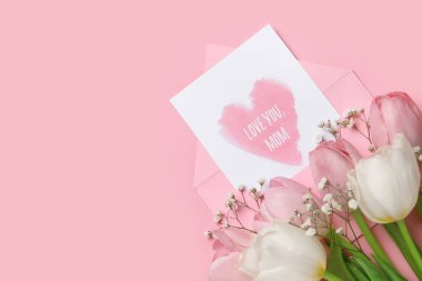 Zarfta şenlikli kartpostal ve pembe arka planda çiçekler. Anneler Günü kutlaması