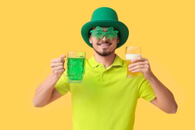 Sarı arka planda birası olan cüce şapkalı mutlu genç adam. Aziz Patrick Günü kutlaması