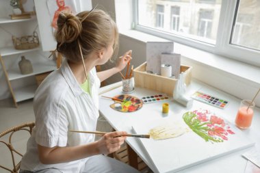 Atölyedeki masada resim yapan kadın sanatçı.