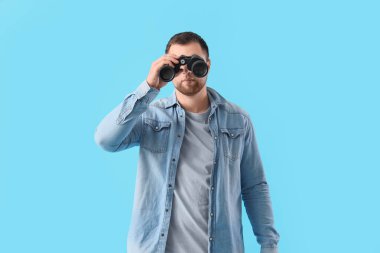 Genç adam mavi arka plandaki dürbünlerden bakıyor.