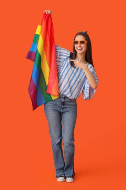 Turuncu arka planda LGBT bayrağını gösteren güzel genç bir kadın.