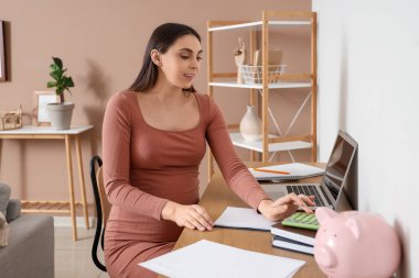 Evde hesap makinesi kullanan hamile bir kadın. Annelik Faydası kavramı