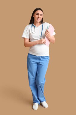 Kahverengi arka planda steteskobu olan güzel hamile bir doktor.