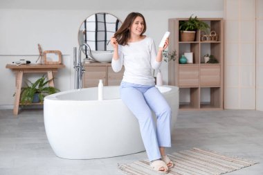 Güzel, genç ve mutlu bir kadın. Banyoda saç yerine bir şişe ürünle.