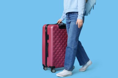 Sırt çantalı ve çantalı genç bir kadın mavi arka planda bir yere gidiyor. Seyahat kavramı