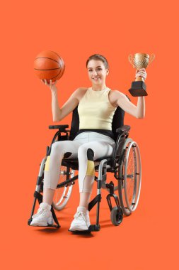 Turuncu arka planda altın kupası olan tekerlekli sandalyedeki bayan basketbolcu.