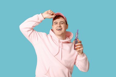 Mavi arka planda bir şişe sodası olan genç adam.