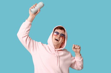 Mavi arka planda bir kutu sodayla güneş gözlüğü takan mutlu genç adam.