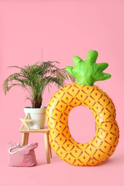 Ananas şeklinde şişirilebilir halka, pembe arka planda ev bitkisi ve çanta.