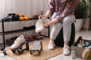 Evde şık spor ayakkabılara su püskürtücü sprey sıkan bir kadın.