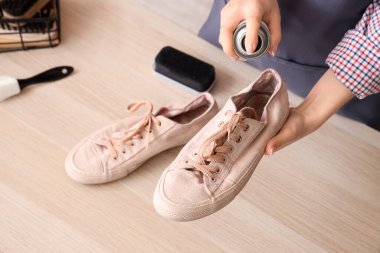 Kadın ayakkabıcı, ahşap masadaki ayakkabıların üzerine su püskürtücü sıkıyor, yakın plan.