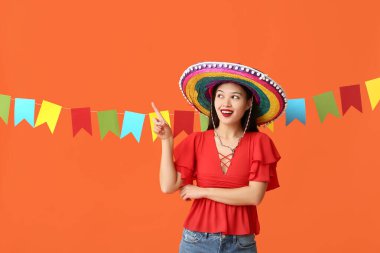 Meksika şapkalı mutlu genç kadın turuncu arka plandaki bir şeyi işaret ediyor.