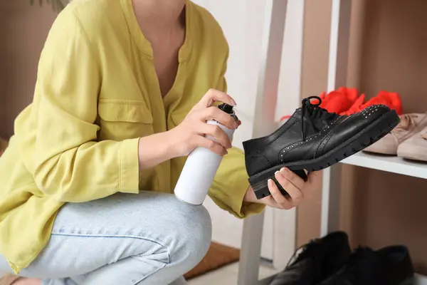 Woman applying water repellent spray on black leather shoe at home