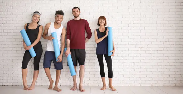 Kelompok Orang Sporty Dengan Tikar Yoga Dekat Dinding Bata Putih Stok Gambar