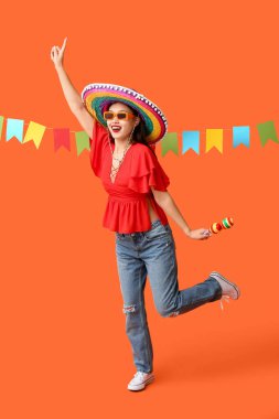 Meksika şapkalı ve turuncu arka planda marakas giyen mutlu genç kadın.