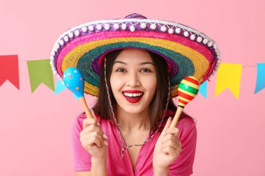 Meksika şapkalı, marakas ve pembe arka planda çelengi olan mutlu genç kadın.