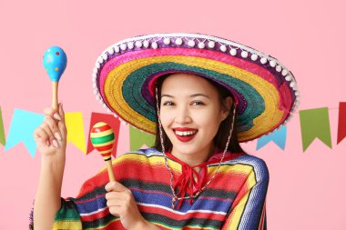 Meksika elbiseli mutlu genç bir kadın, pembe arka planda marakas ve çelenklerle