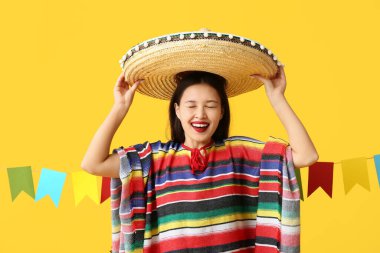 Sarı arka planda Meksika şapkalı ve pançolu mutlu genç kadın.