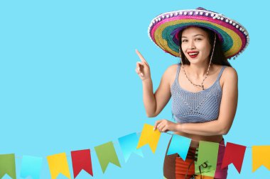 Meksika şapkalı ve çelenkli mutlu genç kadın mavi arka planda bir şeye bakıyor.