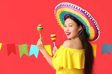 Meksika şapkalı ve kırmızı arka planda marakas giyen mutlu genç kadın.