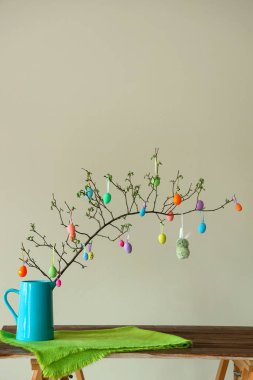Ağaç dalları ve renkli Paskalya yumurtaları olan vazo ışıklı duvarın yanında.